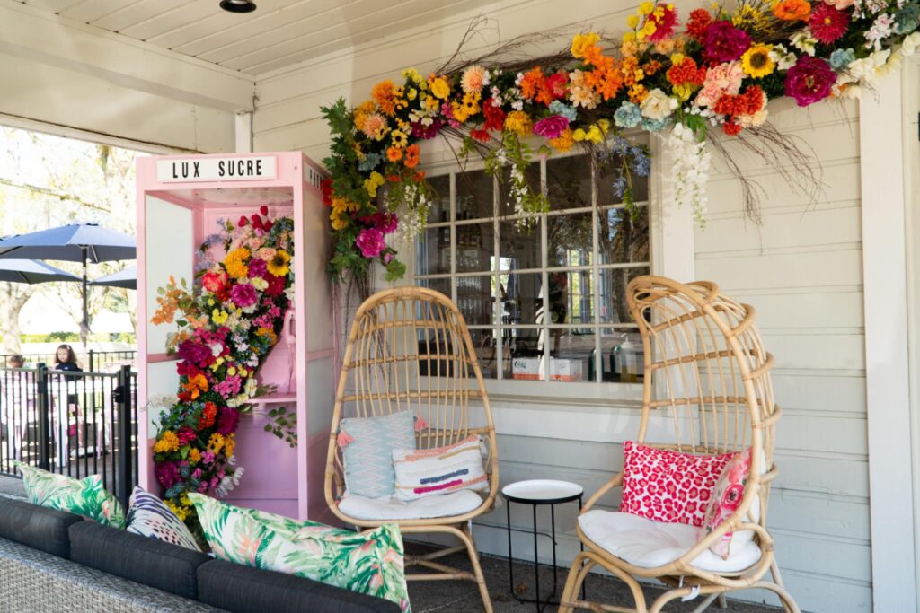 Wooden wicker chairs on a porch next to a pastel pink phone booth with flowers inside
