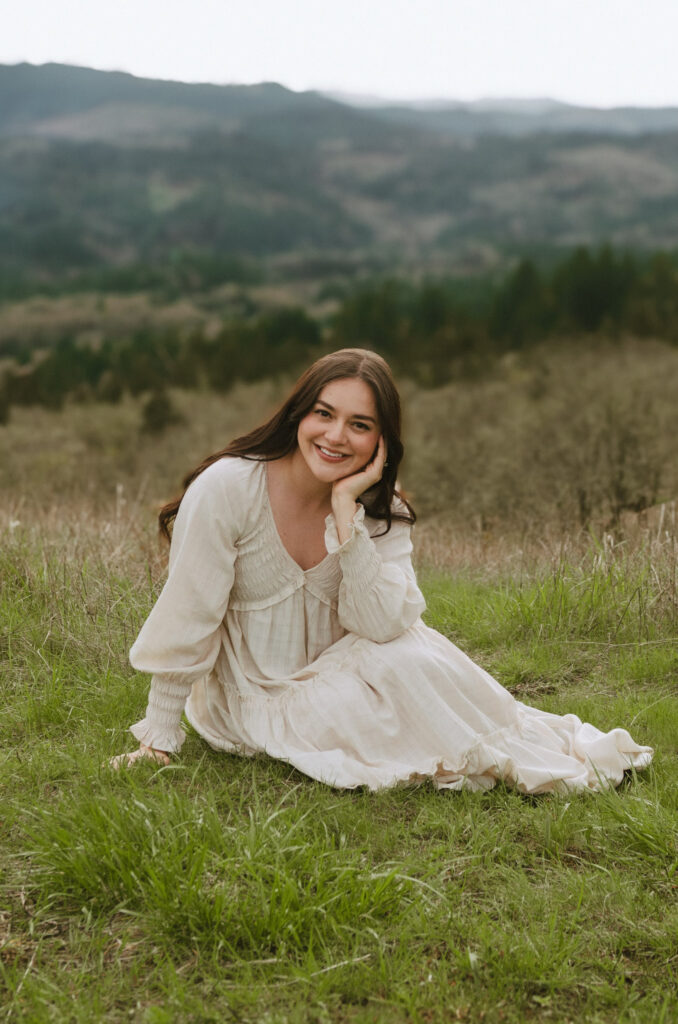 Photo of the blog author, Bri Santos (Wander with Bri), in a white dress laying on the grass in a mountain scene.