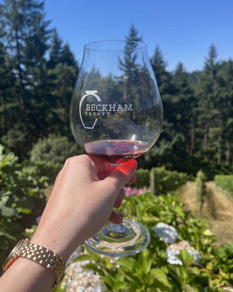 Photo of person holding a glass of wine with the Beckham Estate Vineyard in the background (Must-Do Fall Activities In and Around Wilsonville)