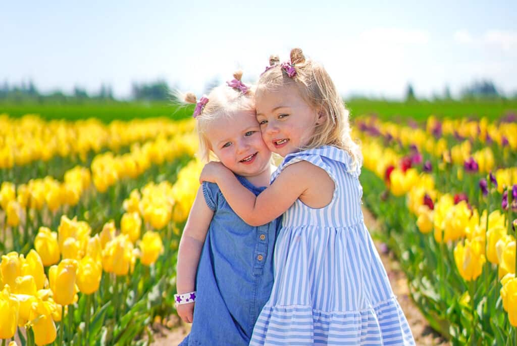 Photo of two little girls in blue dresses embracing while in a field of yellow, red, and pink tulips