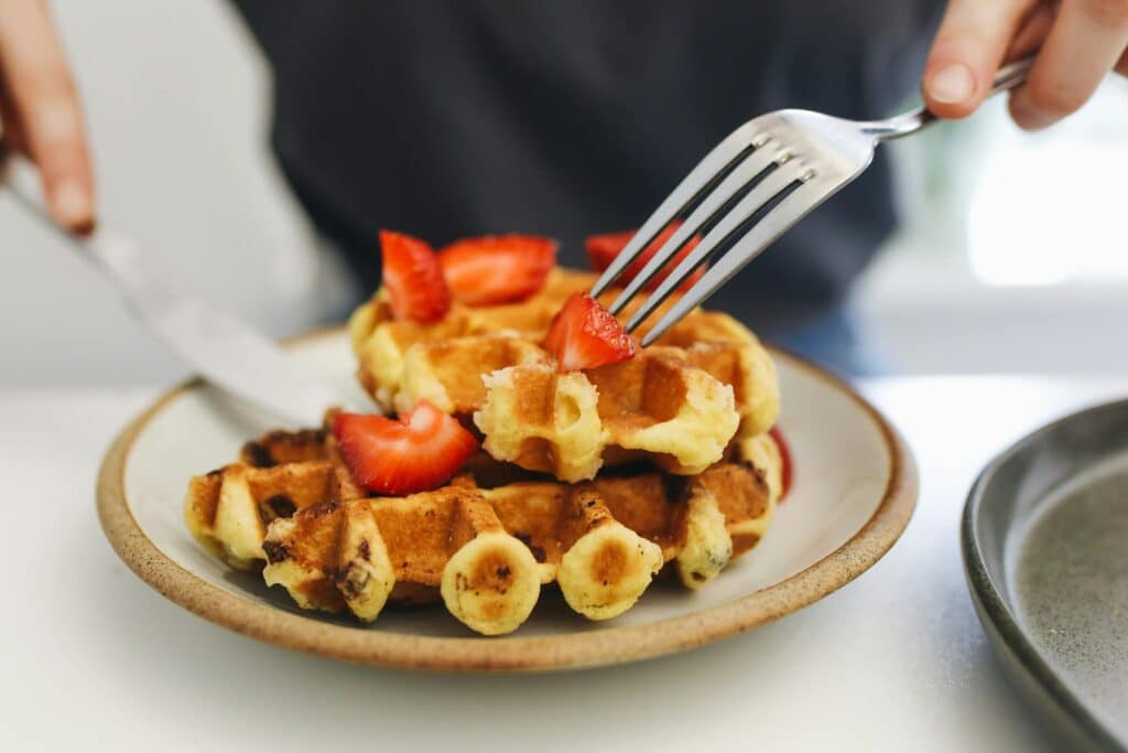 Photo of someone cutting a stack of waffles topped with strawberries during brunch
