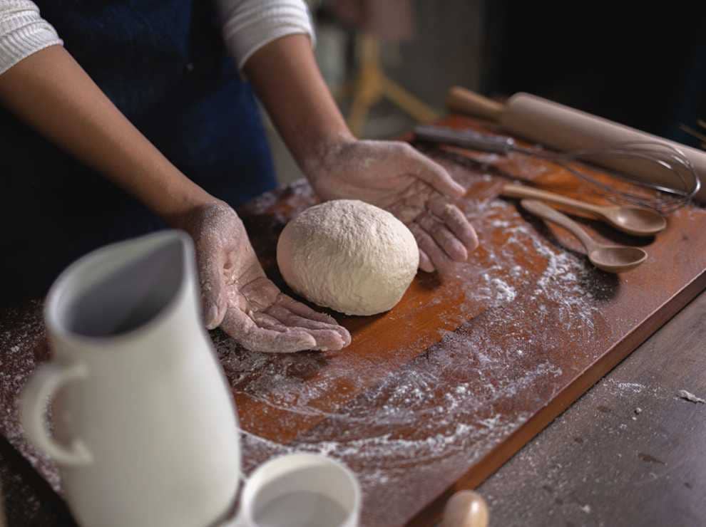 photo of a person rolling dough on the kitchen counter while making bread