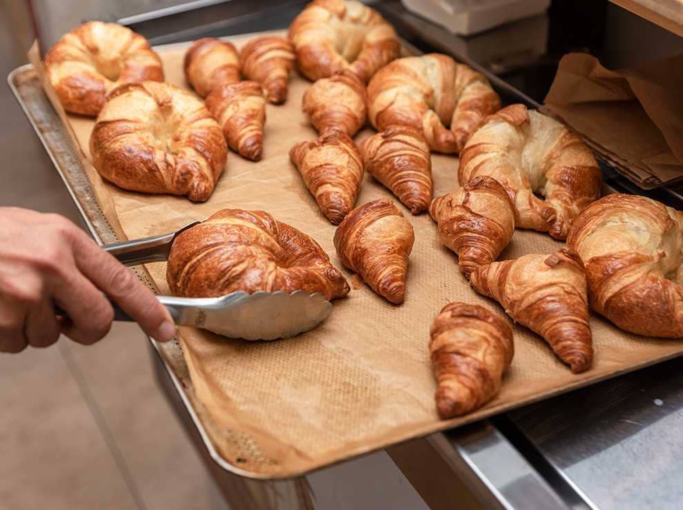 photo of freshly baked golden crispy croissants being pulled from the oven and checked